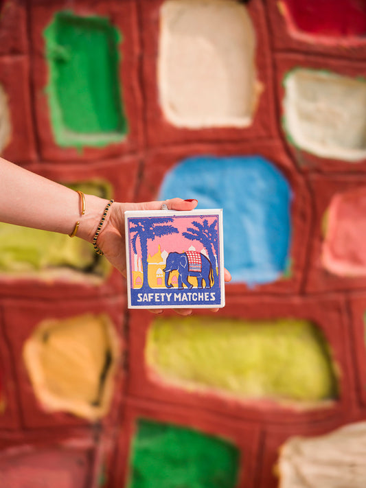 Boîte d’allumettes Pink Elephant Archivist Gallery tenue à la main devant un mur coloré