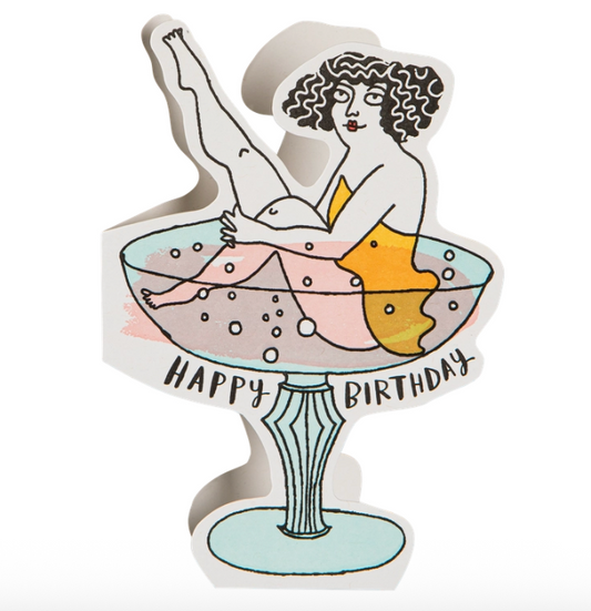 Carte Birthday Cocktail d’Archivist Gallery, illustration letterpress d’un verre de cocktail coloré et pétillant avec une femme aux cheveux boucles assise dedans, elle porte une robe jaune et lève une de ses jambes, style artistique et festif, fond blanc, papier recyclé premium, enveloppe colorée incluse, intérieur vierge prêt à écrire un message.