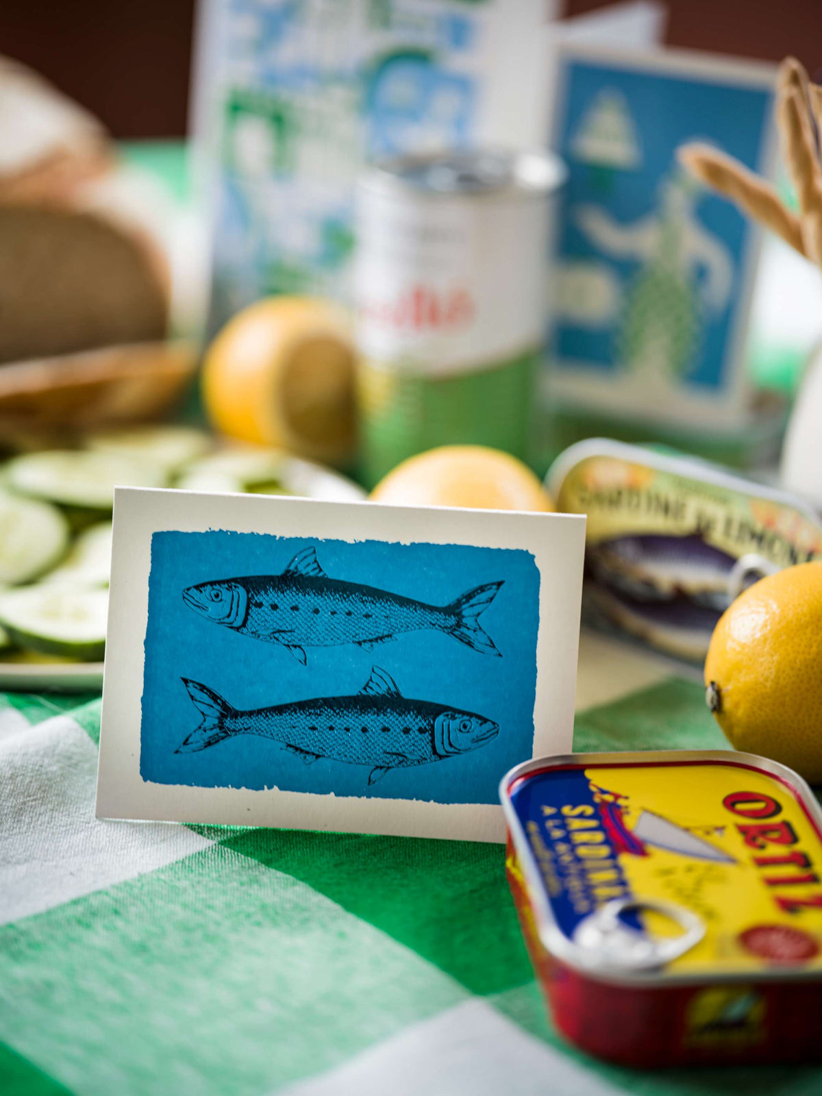 Carte Sardines Archivist Gallery près d’une boîte de sardines, mise en scène sur table