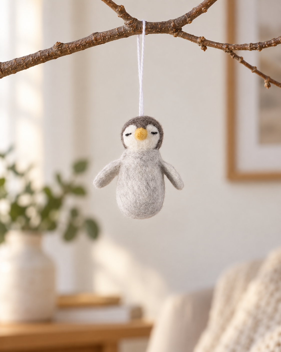 Bébé pingouin Aveva en laine suspendu à une branche, mise en situation reconstituée