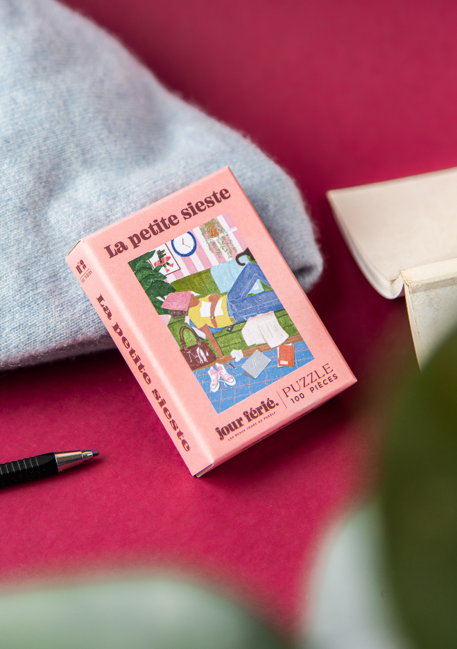 Boîte La petite sieste Jour Férié inclinée près d’un plaid et d’un livre