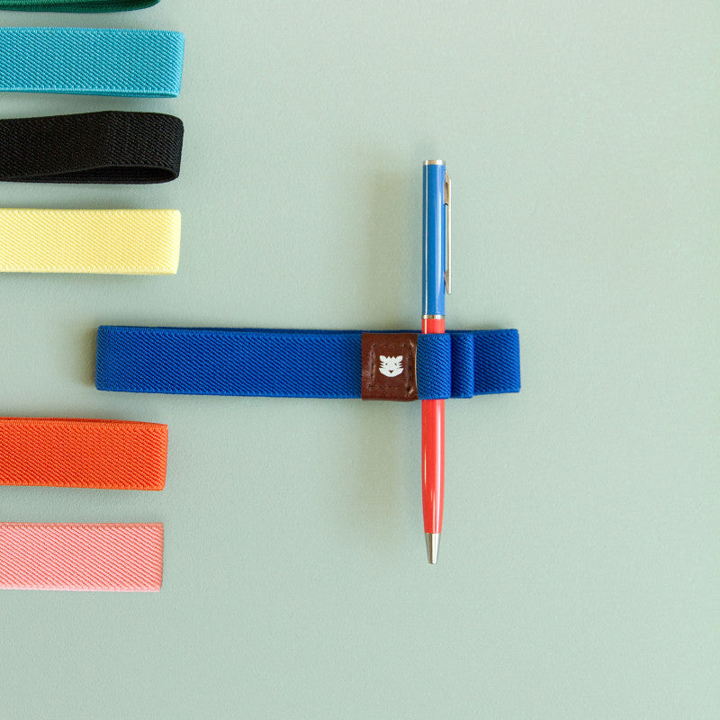 Stylo-bille Bleu-Brique Papier Tigre mis en scène avec un élastique porte-stylos