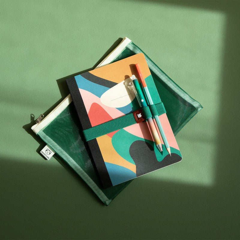 Élastique porte-stylos Le Voyageur vert Papier Tigre mis en scène avec des carnets